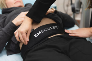 Emsculpt Neo body contouring treatment at CATARA Medical Spa in Algonquin showing the device applicator positioned on a client's abdomen during a non-invasive muscle building and fat reduction session