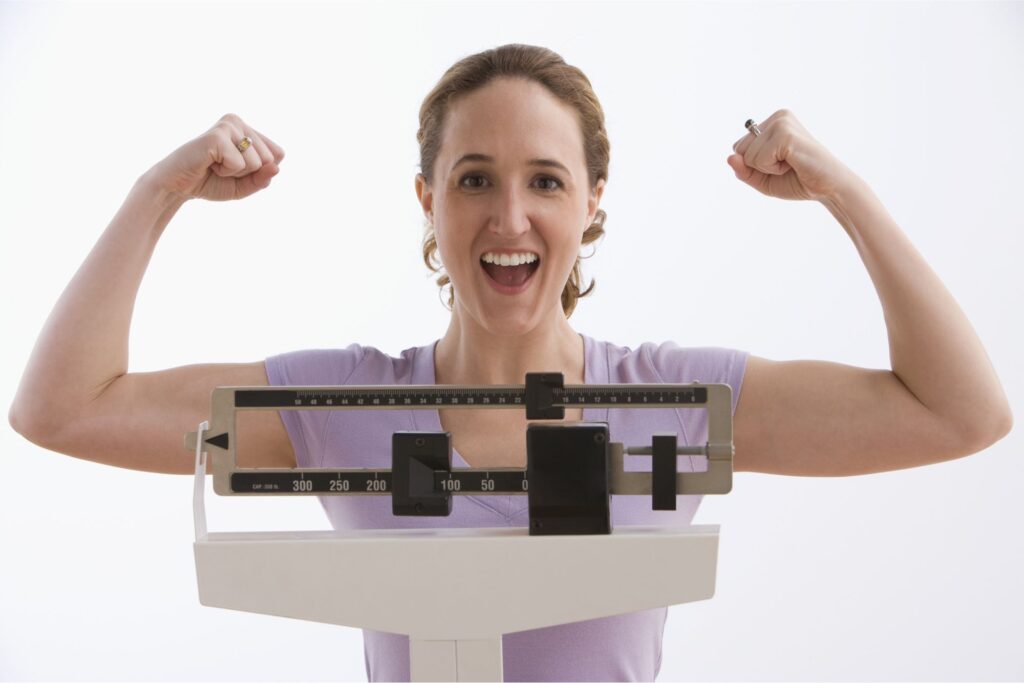 happy woman flexing muscles after weight loss success on scale at catara med spa algonquin il semaglutide and body transformation program