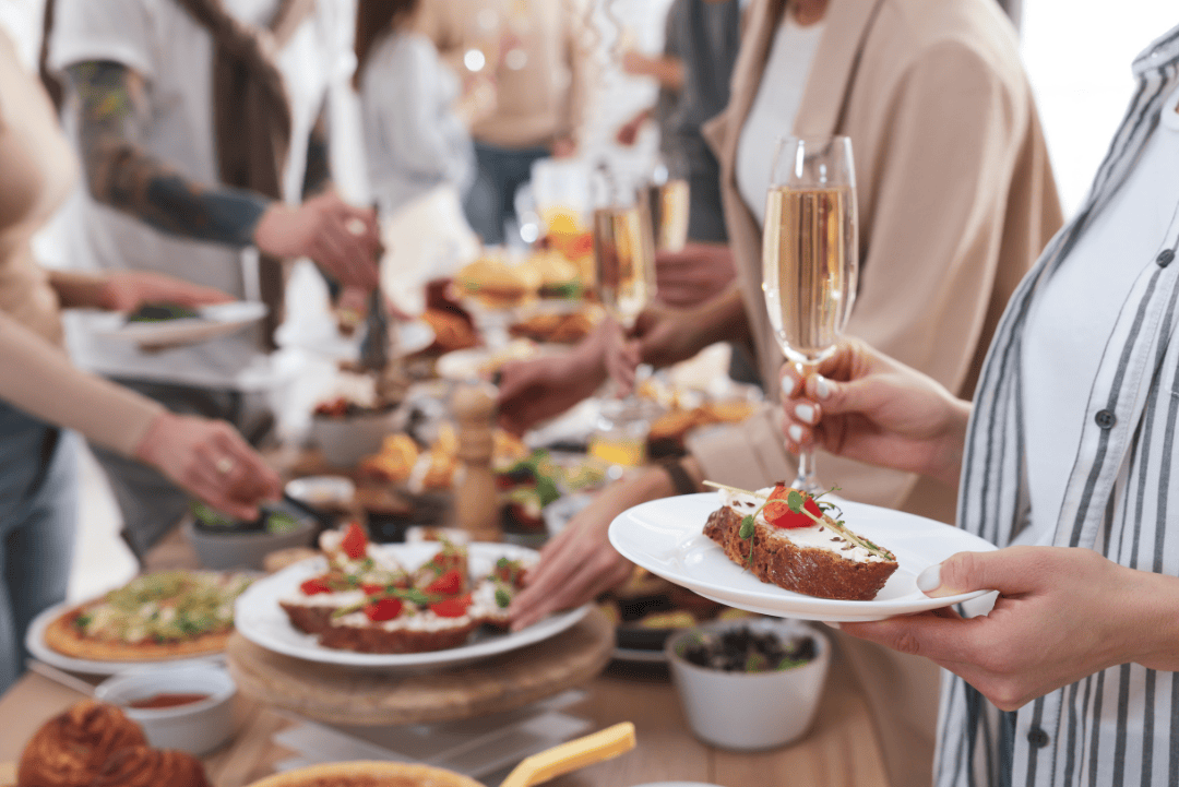 Holiday buffet table with guests holding champagne and healthy appetizers, promoting mindful seasonal eating habits.