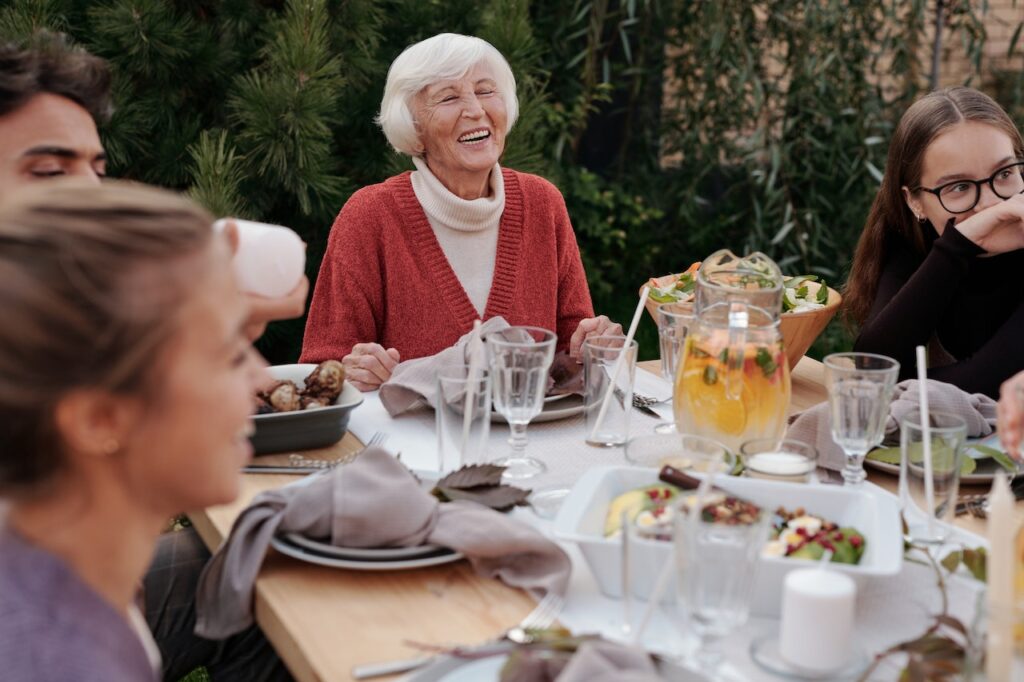 Older woman with visible crepey skin on arms enjoying outdoor family meal in Algonquin summer light.